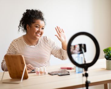 Cheerful beauty blogger with makeup product recording video on smartphone