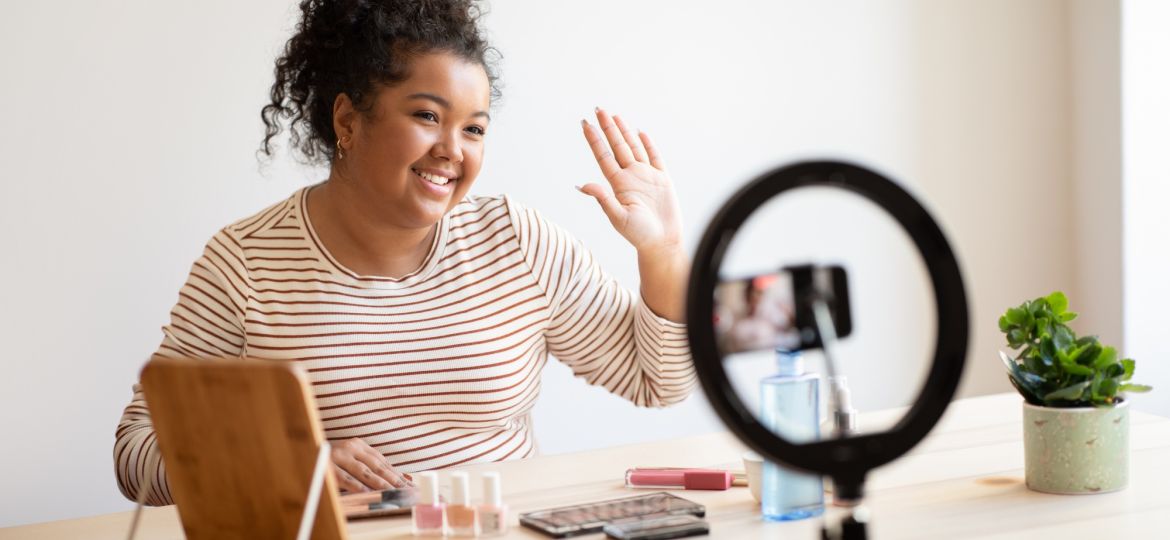 Cheerful beauty blogger with makeup product recording video on smartphone