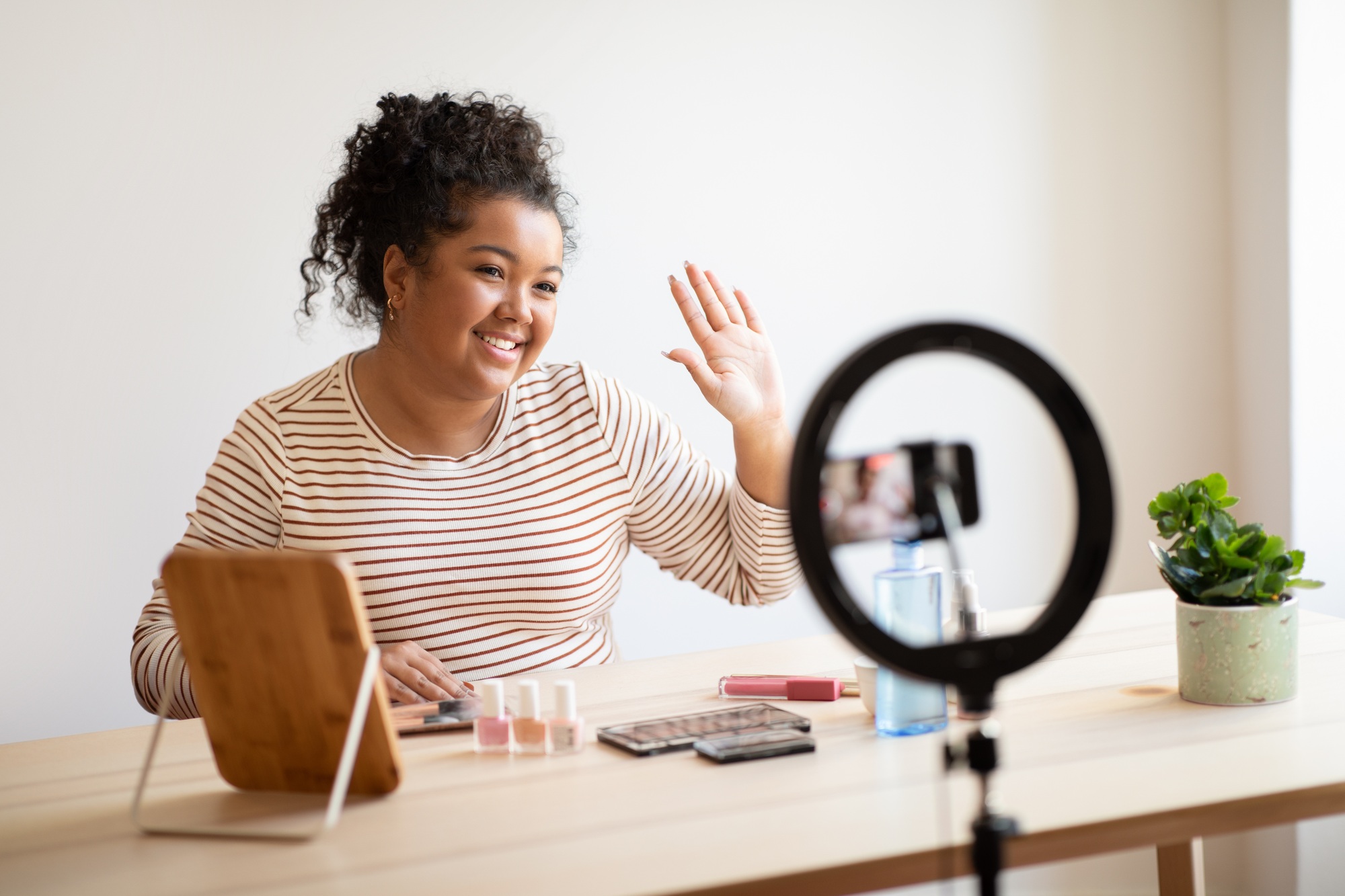 Cheerful beauty blogger with makeup product recording video on smartphone